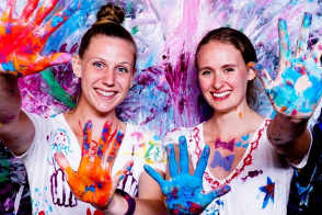 Two women covered in paint during a "Paint for Swag" event.