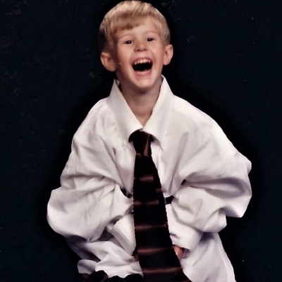 A young blake dressed in an an adult-sized dress shirt and tie.